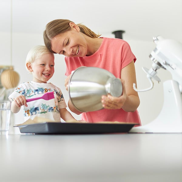 Moeder en kind aan het lachen in de keuken terwijl ze aan het bakken zijn met een keukenrobot