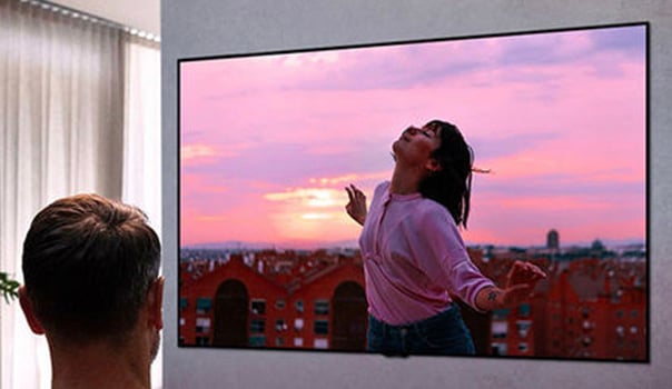 Un homme regarde la tlvision avec une femme dansant sur l'cran pendant le coucher du soleil.