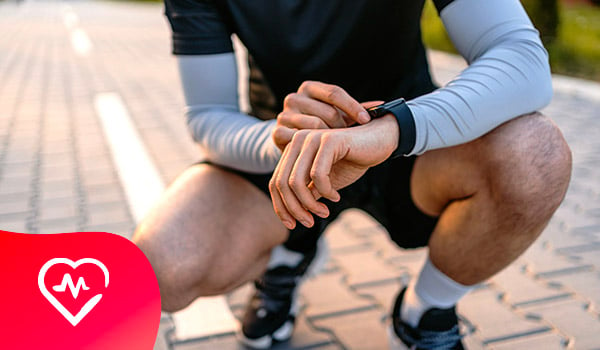 Een man in sportieve kledij hurkt om zijn smartwatch te raadplegen.