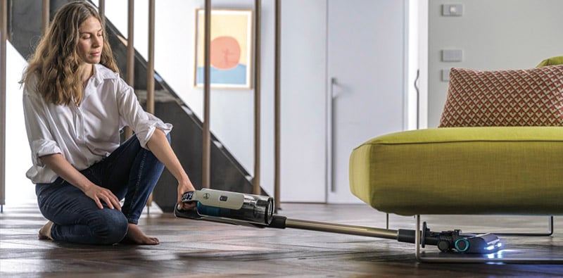 Een vrouw die onder haar zetel stofzuigt met de Hoover HF9 steelstofzuiger