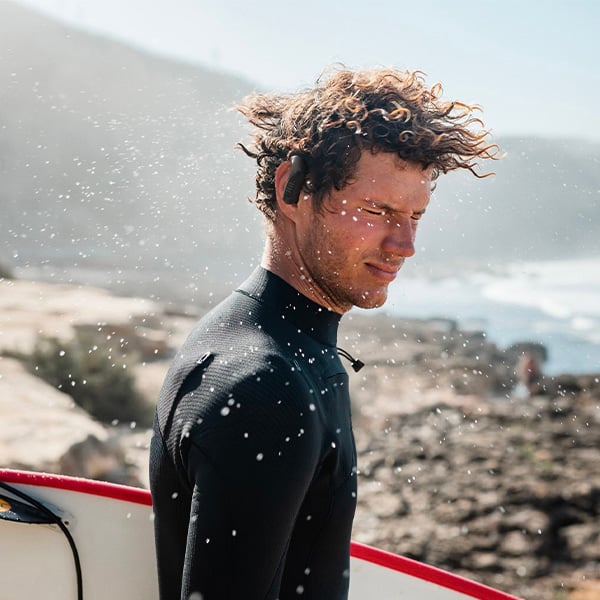 Un homme qui porte ses couteurs sans fil et sa planche de surf  