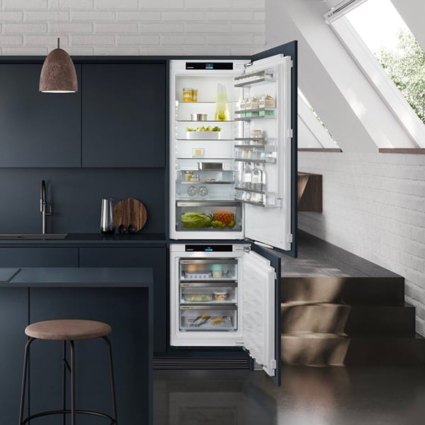 Un combi frigo conglateur  encastrable noir ouvert dans une cuisine bleu et blanc 