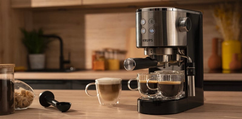 Krups Virtuoso espressomachine op een keukentafel met 3 kopjes koffie