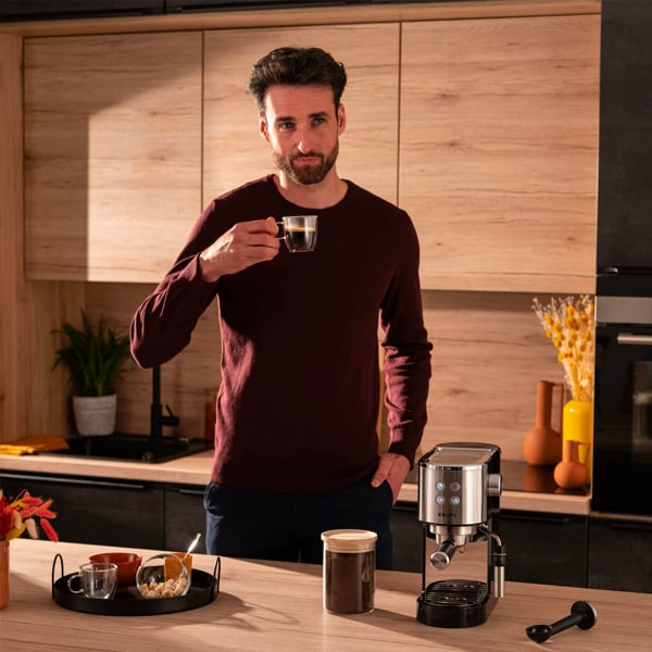 Een dertiger staat in zijn keuken met een kopje koffie in zijn handoffie gaat drinken