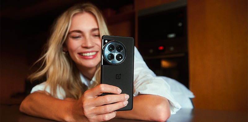 Une dame blonde souriante qui utilise son OnePlus noir