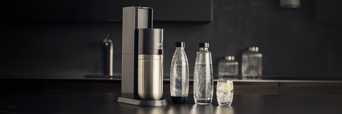 Een Sodastream Duo Black apparaat, twee flessen en een glas gevuld met bruisend water, in een donkere keuken.