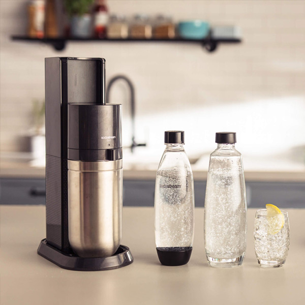 Een Sodastream Duo Black apparaat, twee flessen en een glas gevuld met bruisend water, in een lichte keuken