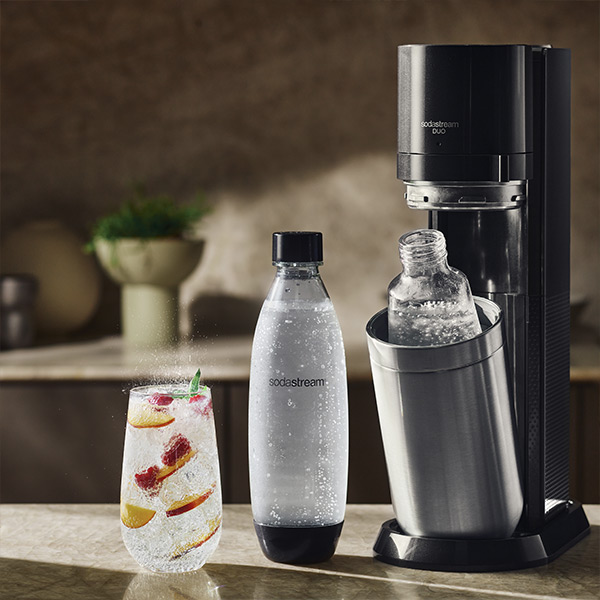 Inzoomen op de Sodastream Duo Black machine, de twee flessen en een glas bruiswater gevuld met vers fruit