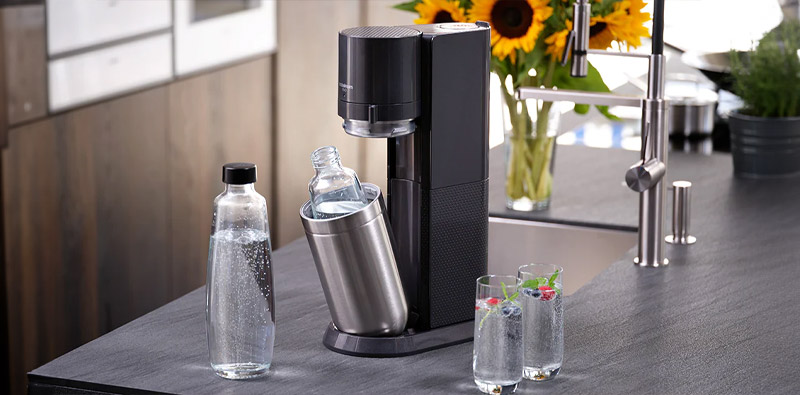 Een Sodastream Duo Black apparaat, twee flessen en twee glazen gevuld met bruisend water, in een lichte keuken.