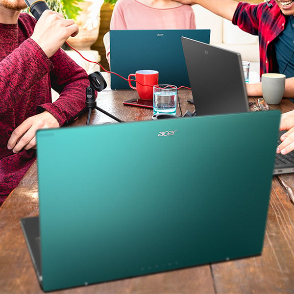 Des PC portables Acer Aspire bleu, gris et vert sur une table  manger en bois entoure de 3 personnes, un microphone est connect  l'un des PC